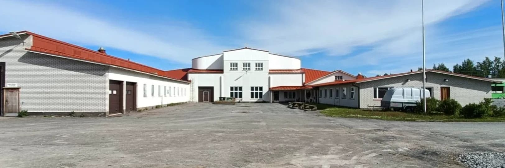 Panorama of the Forsnäs Energy Park property, with long brick buildings on both sides of a paved yard and the white central building with a red roof.